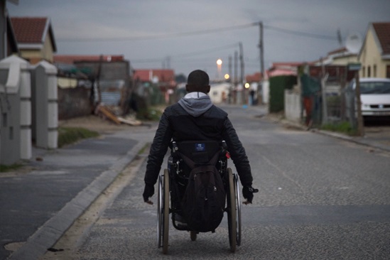 A man driving his wheelchair on a street in the evening
